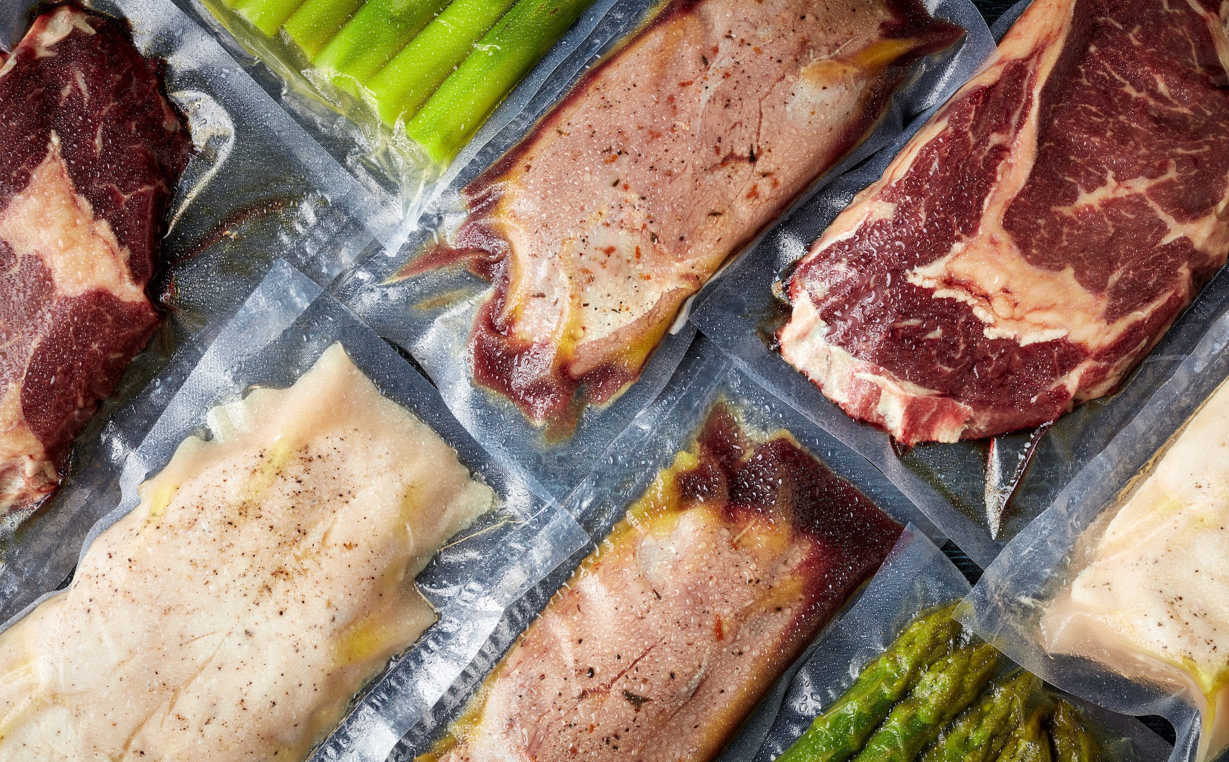Meat and asparagus vacuum sealed on black table, from above